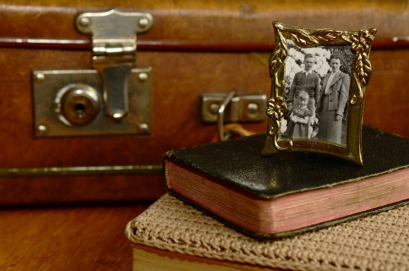 Altes Familienfoto in einem Goldrahmen auf einem Buch, im Hintergrund ein brauner Lederkoffer – symbolisch für Ahnenarbeit und familiäres Erbe