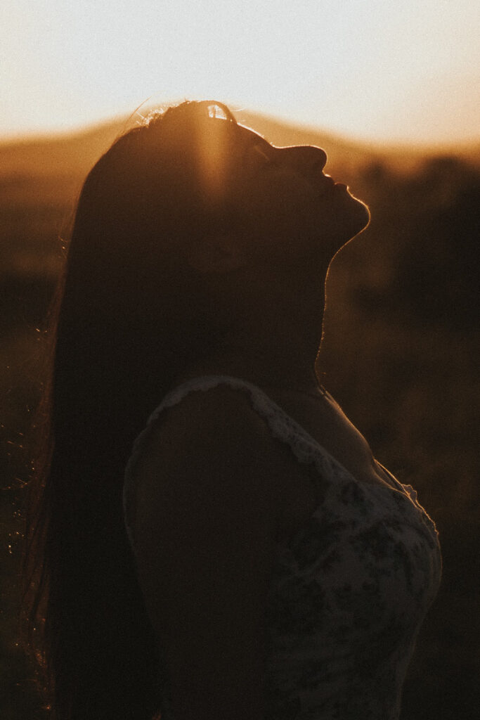 Silhouette einer Frau im warmen Abendlicht, Kopf leicht nach oben gerichtet, von einem Sonnenstrahl berührt – Symbol für spirituelle Verbindung und inneren Dialog.