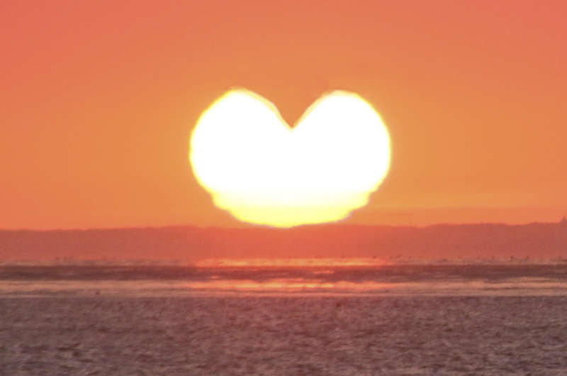 Die untergehende Sonne erscheint in Herzform über dem Meer. Ein leuchtendes Naturschauspiel, das für Liebe, Lichtkraft und schöpferische Energie steht.