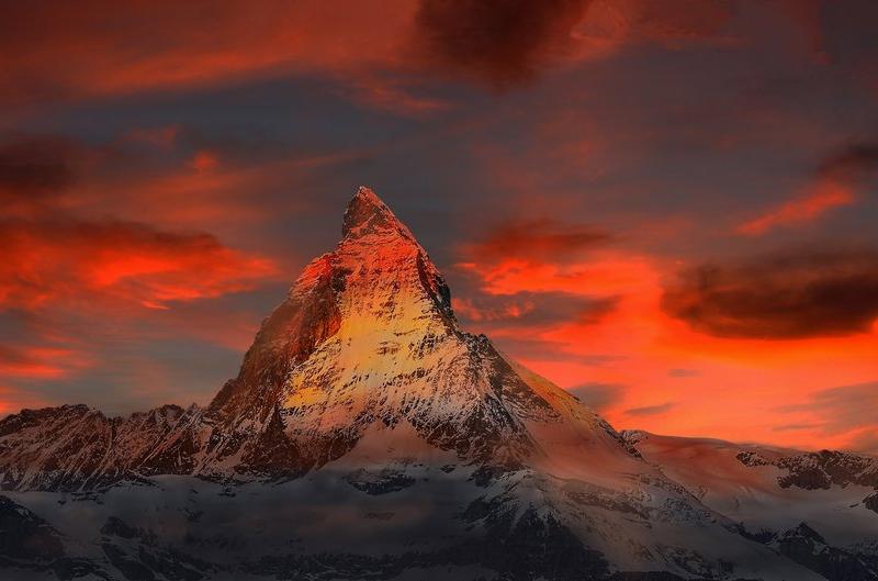 Schroffer, schneebedeckter Berggipfel im Abendrot, das Matterhorn leuchtet vor dramatisch rotem Himmel – Symbolbild für ein intensives Peak-Erlebnis im Gegensatz zum Alltag.