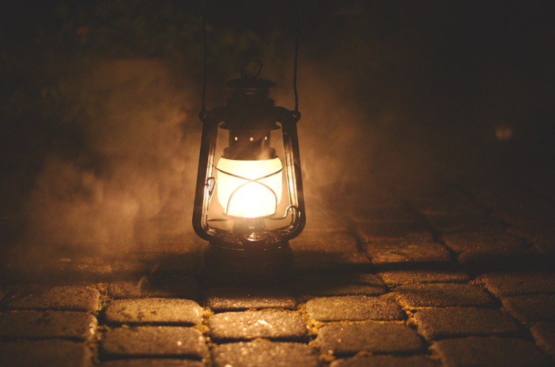 Alte Laterne leuchtet im Dunkeln auf Kopfsteinpflaster und wirft warmes Licht in den Nebel – Symbol für Klarheit in verwirrenden Beziehungen und Gaslighting.