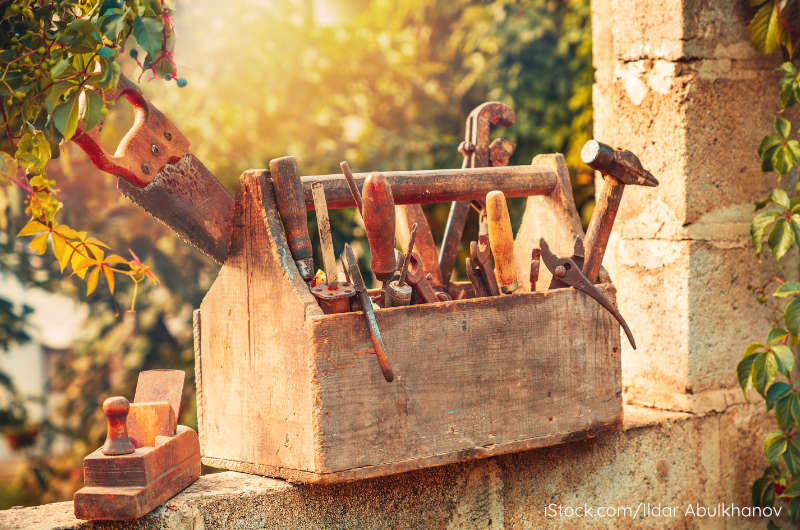 Alte Holzkiste mit Handwerkzeugen im warmen Sonnenlicht vor grünem Hintergrund – Symbol für innere Heilungswerkzeuge und den Weg ins Leben.